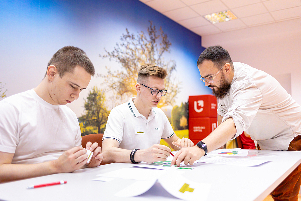 dwoje studentów siedzących przy stole dyskutuje z trenerem